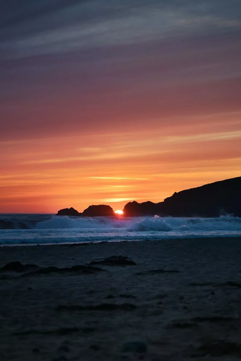 The sun is setting over the ocean with a beach in the foreground
